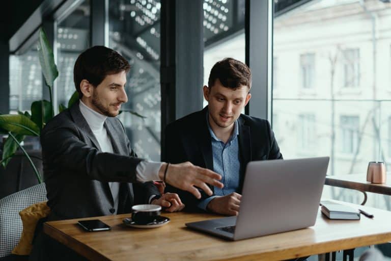 two businessmen pointing laptop screen while discussing